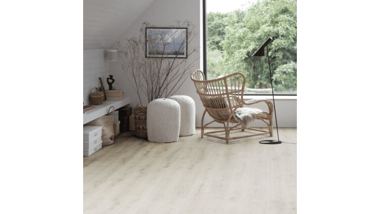 Hell eingerichteter Raum mit Korbsessel, zwei weißen Hockern und großer Fensterfront.